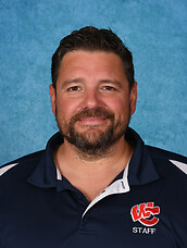 Headshot portrait of Byron Helt smiling against a blue studio background, wearing a navy blue West Central Staff polo shirt.